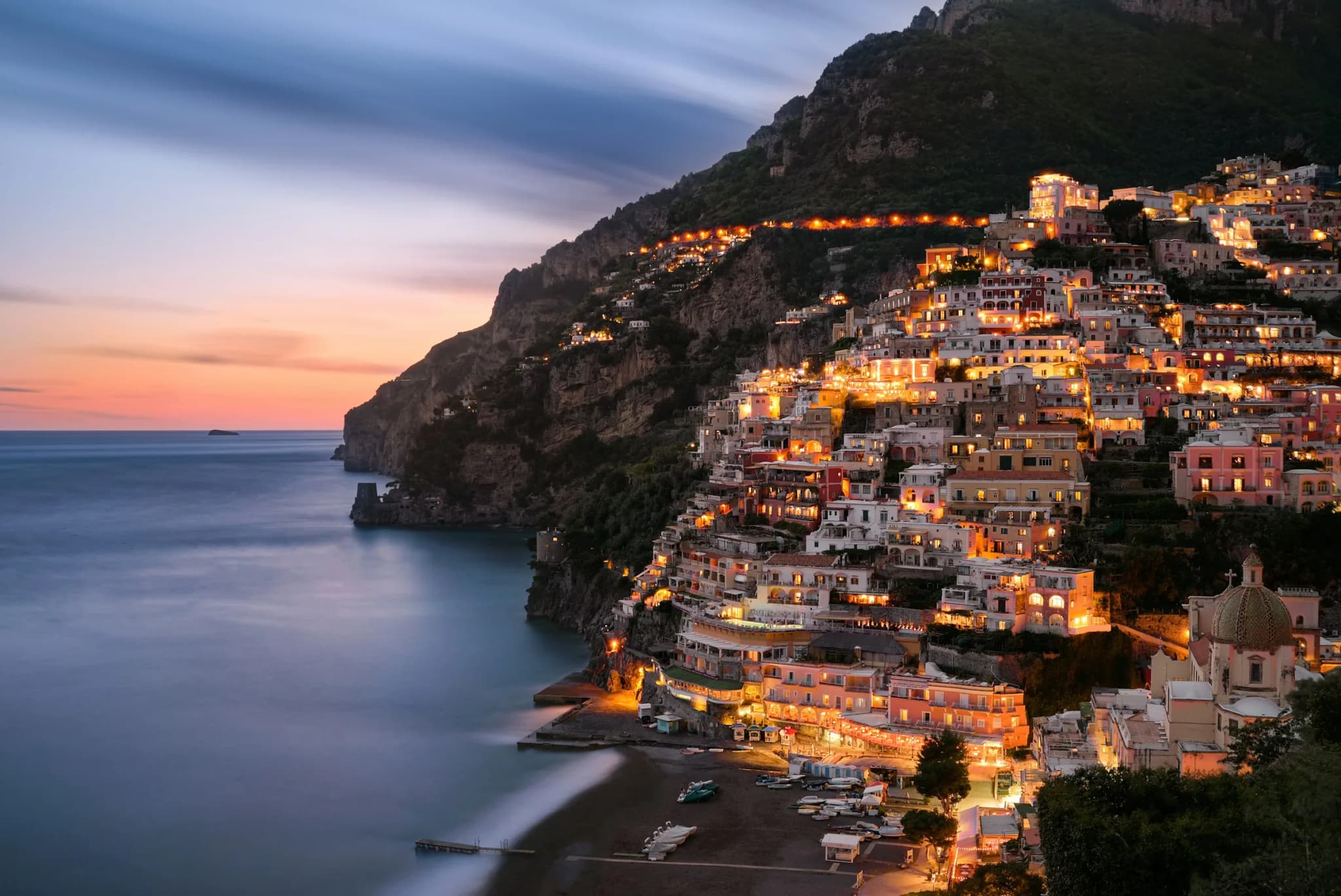 Positano at dusk, windows lit and the sea smoothed by a long exposure