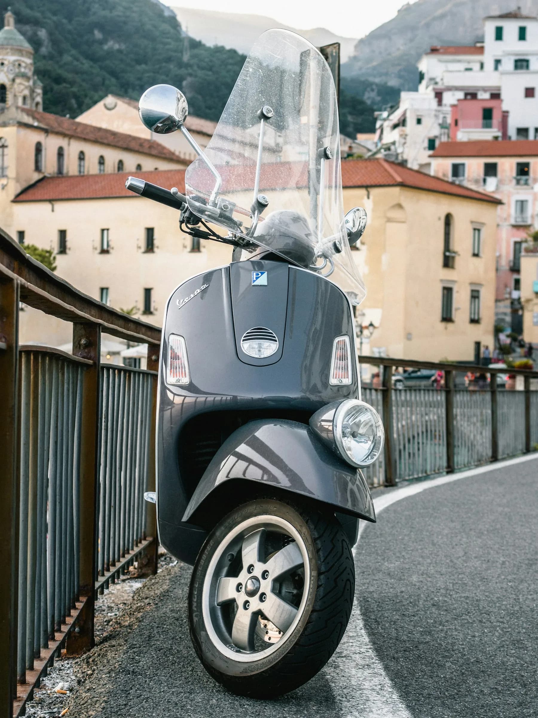 A Vespa parked at the roadside, the town’s houses behind