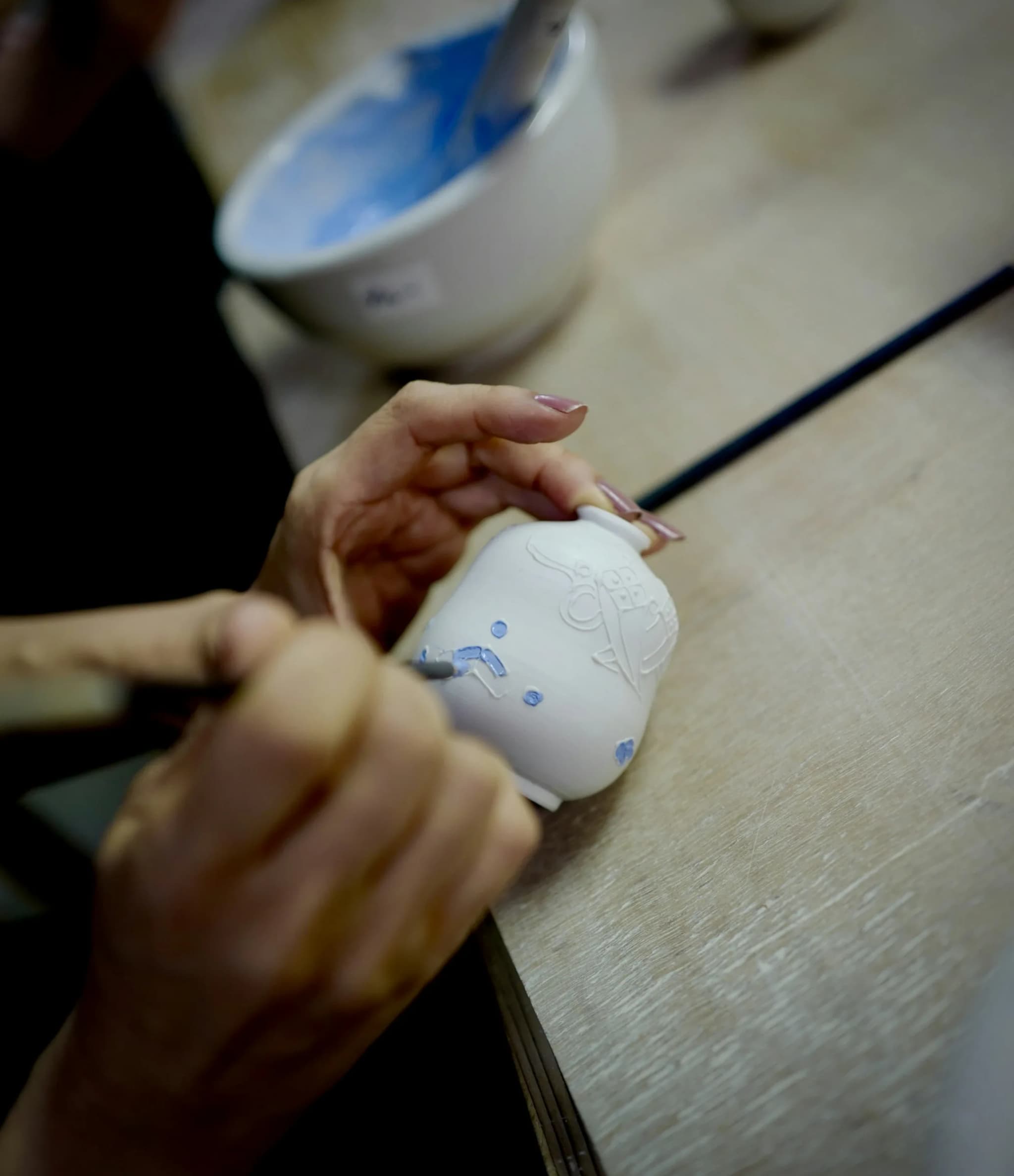 A hand painting a ceramic cup in blue
