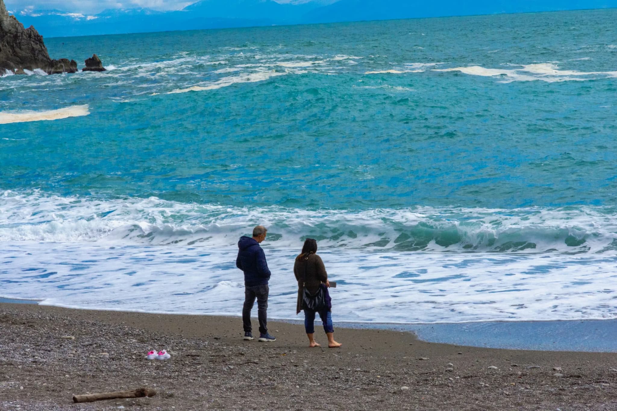 Two people on the shore in front of winter waves